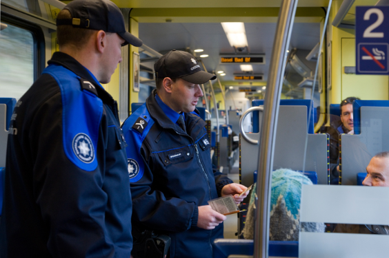Zwei Grenzwächter kontrollieren den Ausweis eines Bahnreisenden.
